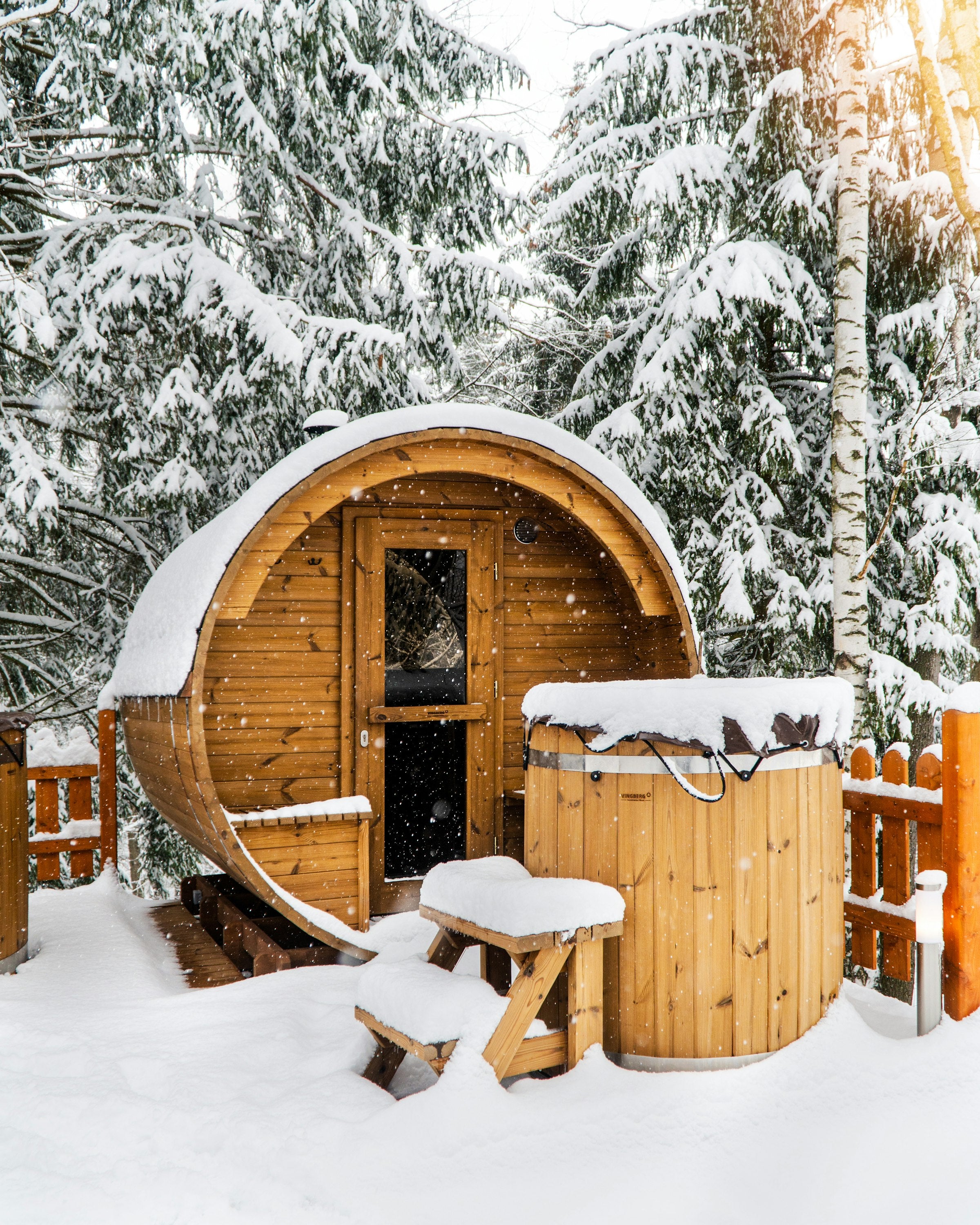 A cedar barrel sauna under snow-laden evergreens in winter light